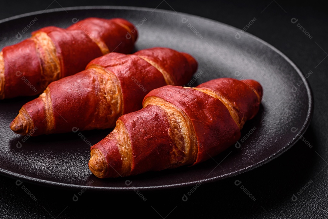 Delicioso croissant vermelho crocante e doce com recheio de creme sobre fundo de concreto texturizado escuro