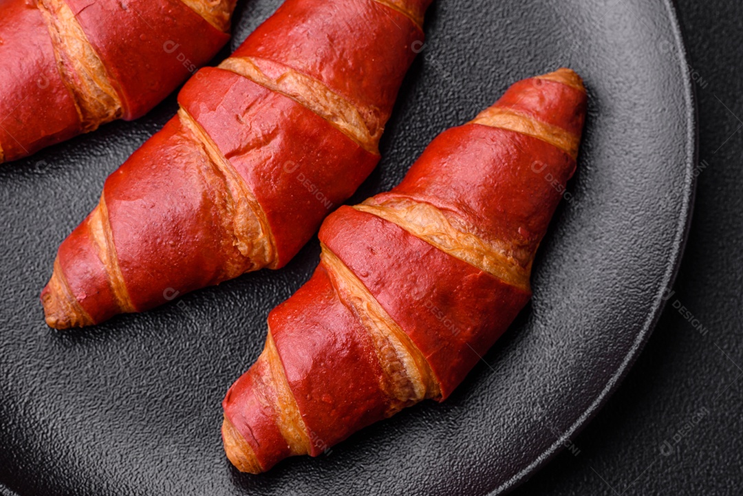 Delicioso croissant vermelho crocante e doce com recheio de creme sobre fundo de concreto texturizado escuro
