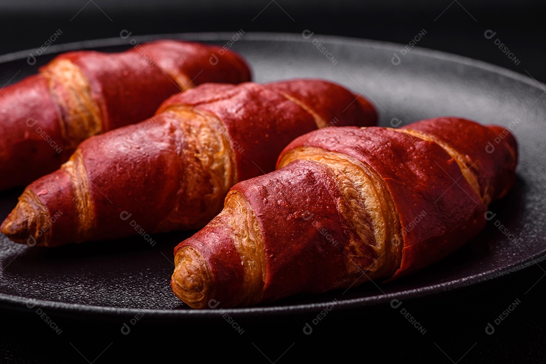 Delicioso croissant vermelho crocante e doce com recheio de creme sobre fundo de concreto texturizado escuro