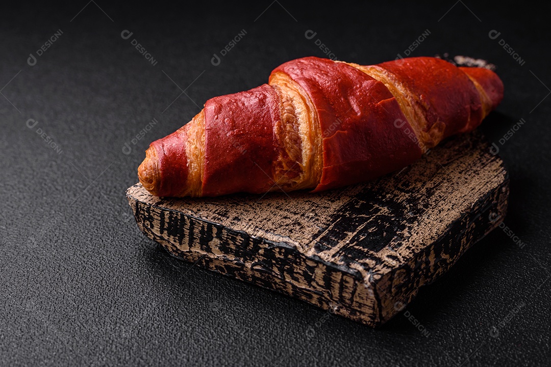 Delicioso croissant vermelho crocante e doce com recheio de creme sobre fundo de concreto texturizado escuro