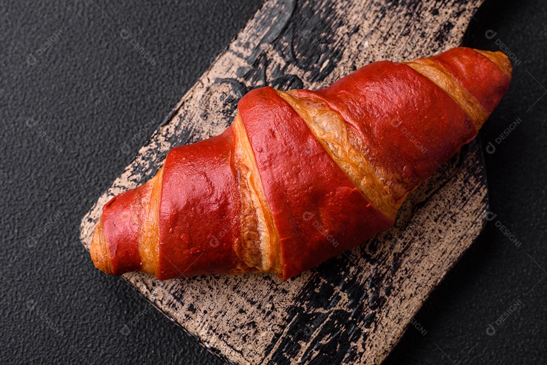 Delicioso croissant vermelho crocante e doce com recheio de creme sobre fundo de concreto texturizado escuro