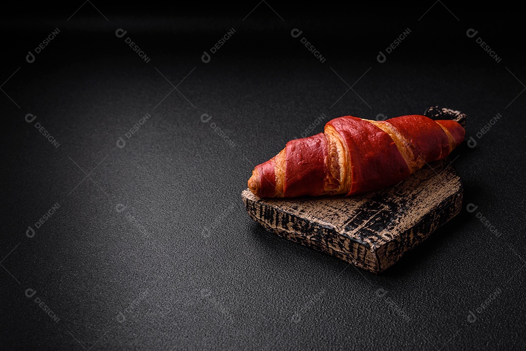 Delicioso croissant vermelho crocante e doce com recheio de creme sobre fundo de concreto texturizado escuro