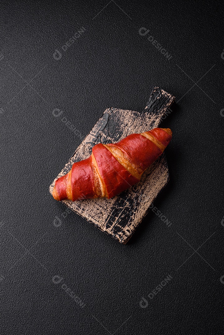 Delicioso croissant vermelho crocante e doce com recheio de creme sobre fundo de concreto texturizado escuro