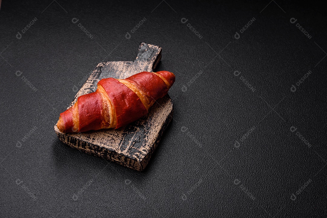 Delicioso croissant vermelho crocante e doce com recheio de creme sobre fundo de concreto texturizado escuro