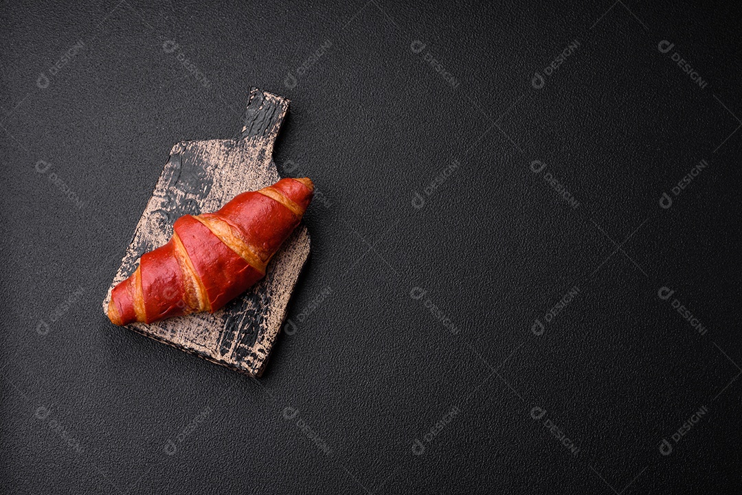 Delicioso croissant vermelho crocante e doce com recheio de creme sobre fundo de concreto texturizado escuro
