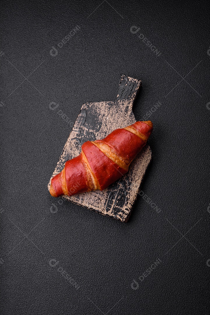 Delicioso croissant vermelho crocante e doce com recheio de creme sobre fundo de concreto texturizado escuro