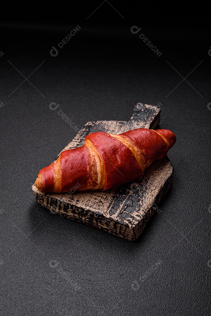 Delicioso croissant vermelho crocante e doce com recheio de creme sobre fundo de concreto texturizado escuro