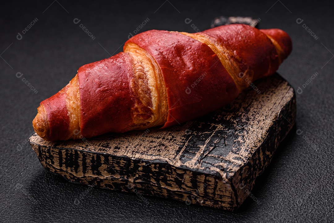 Delicioso croissant vermelho crocante e doce com recheio de creme sobre fundo de concreto texturizado escuro