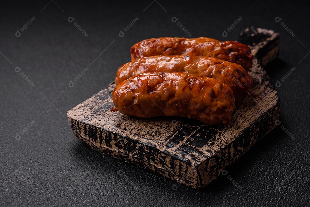 Deliciosas salsichas grelhadas suculentas com sal, especiarias e ervas sobre um fundo escuro de concreto