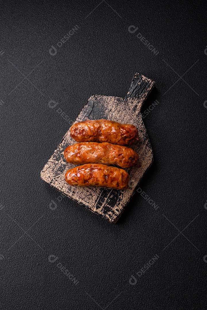 Deliciosas salsichas grelhadas suculentas com sal, especiarias e ervas sobre um fundo escuro de concreto