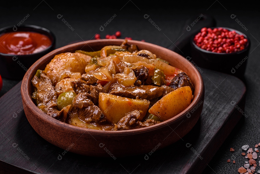Delicioso guisado fresco de batatas, tomates, cebolas, cenouras e carne bovina com sal, especiarias e ervas sobre um fundo escuro de concreto