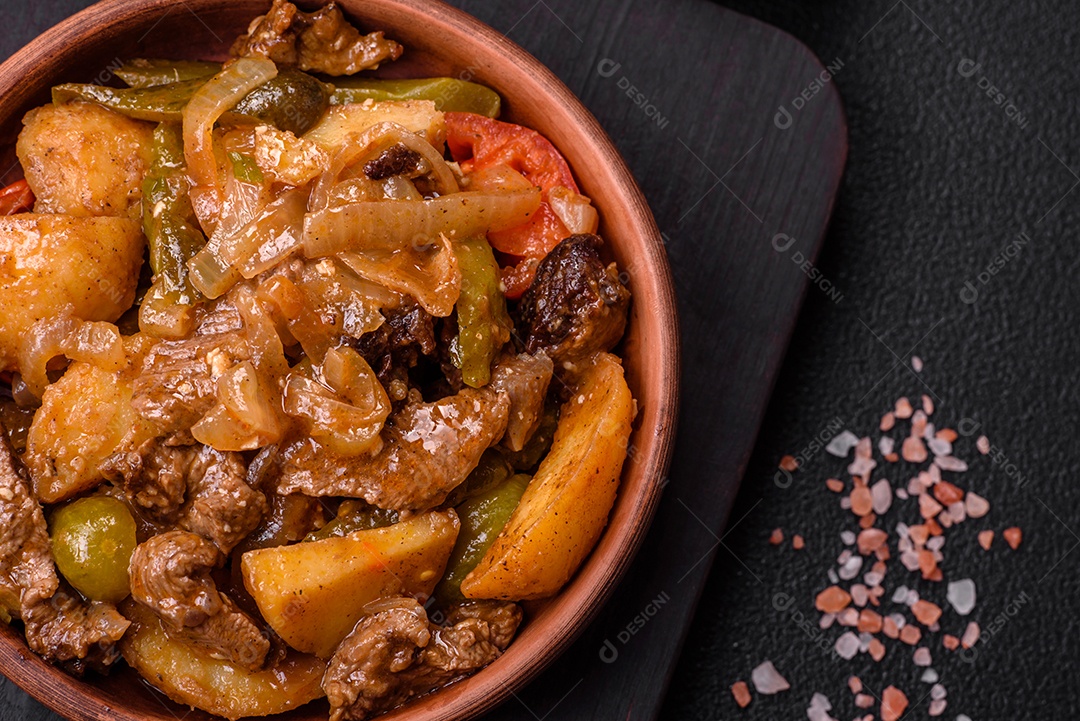 Delicioso guisado fresco de batatas, tomates, cebolas, cenouras e carne bovina com sal, especiarias e ervas sobre um fundo escuro de concreto