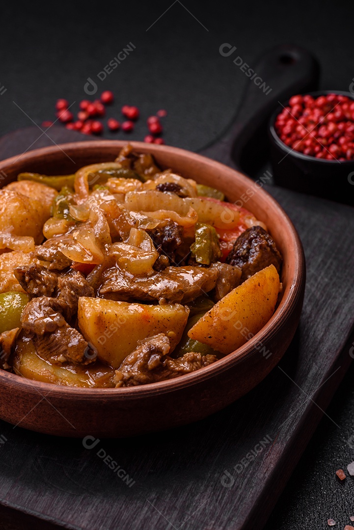 Delicioso guisado fresco de batatas, tomates, cebolas, cenouras e carne bovina com sal, especiarias e ervas sobre um fundo escuro de concreto