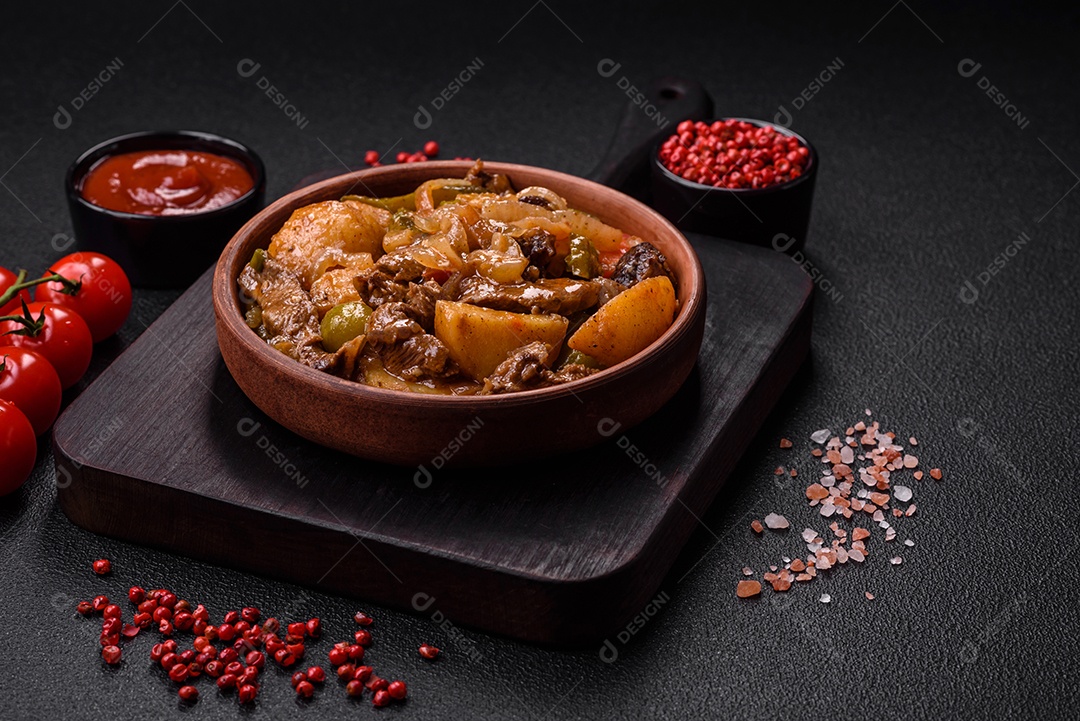 Delicioso guisado fresco de batatas, tomates, cebolas, cenouras e carne bovina com sal, especiarias e ervas sobre um fundo escuro de concreto