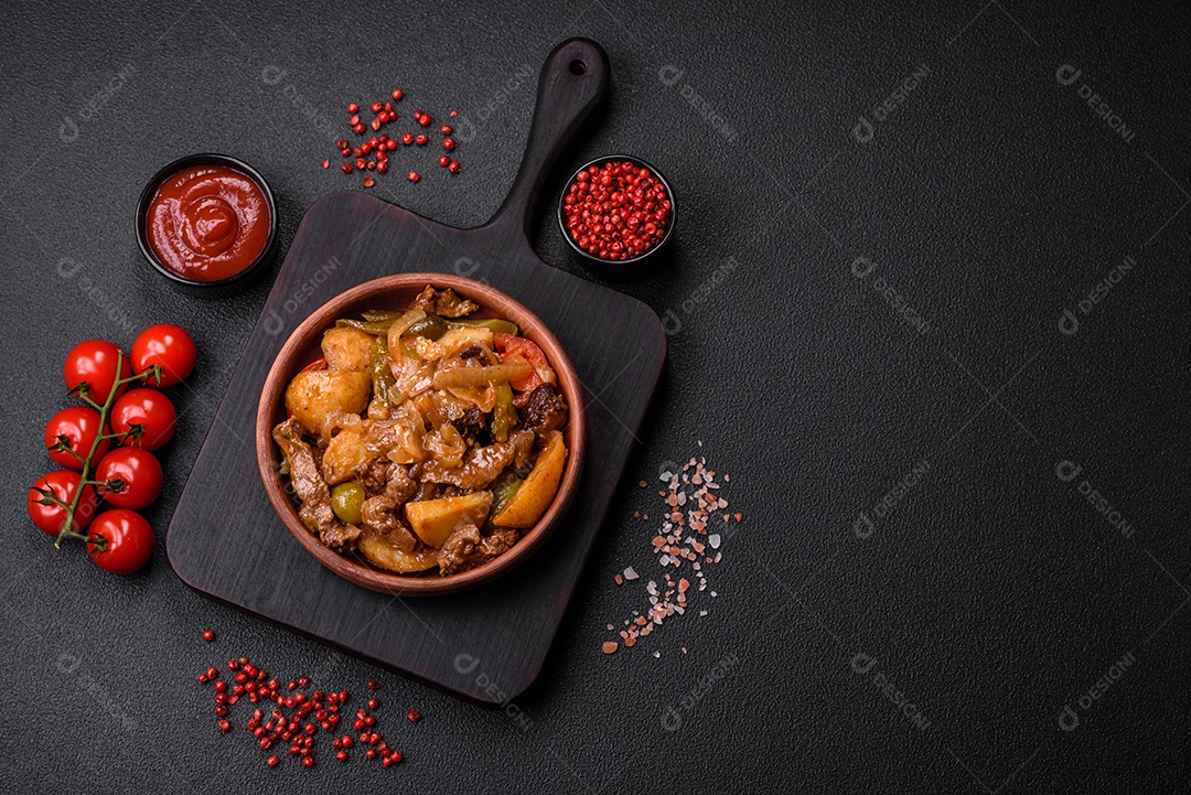 Delicioso guisado fresco de batatas, tomates, cebolas, cenouras e carne bovina com sal, especiarias e ervas sobre um fundo escuro de concreto