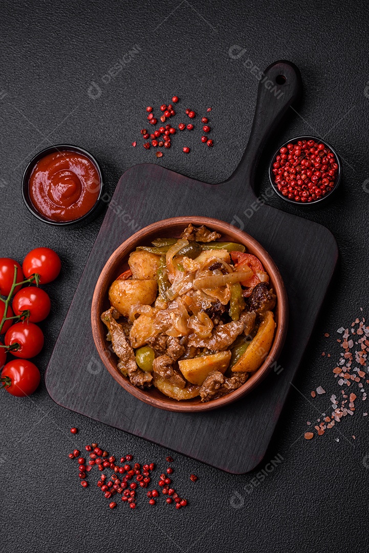 Delicioso guisado fresco de batatas, tomates, cebolas, cenouras e carne bovina com sal, especiarias e ervas sobre um fundo escuro de concreto