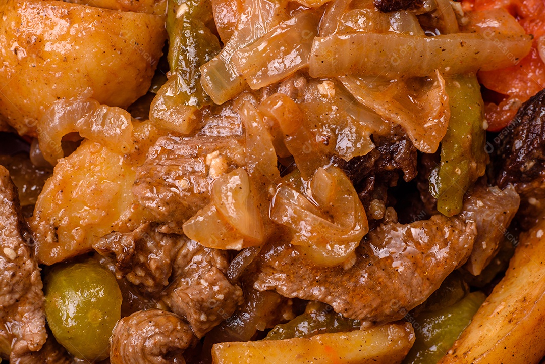 Delicioso guisado fresco de batatas, tomates, cebolas, cenouras e carne bovina com sal, especiarias e ervas sobre um fundo escuro de concreto