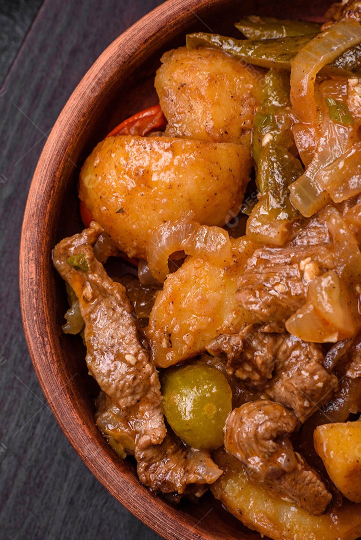Delicioso guisado fresco de batatas, tomates, cebolas, cenouras e carne bovina com sal, especiarias e ervas sobre um fundo escuro de concreto