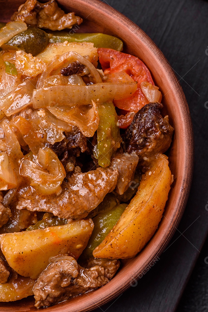 Delicioso guisado fresco de batatas, tomates, cebolas, cenouras e carne bovina com sal, especiarias e ervas sobre um fundo escuro de concreto