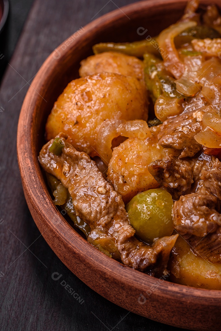 Delicioso guisado fresco de batatas, tomates, cebolas, cenouras e carne bovina com sal, especiarias e ervas sobre um fundo escuro de concreto