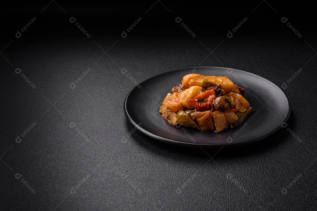Delicioso guisado fresco de batatas, tomates, cebolas, cenouras e carne bovina com sal, especiarias e ervas sobre um fundo escuro de concreto