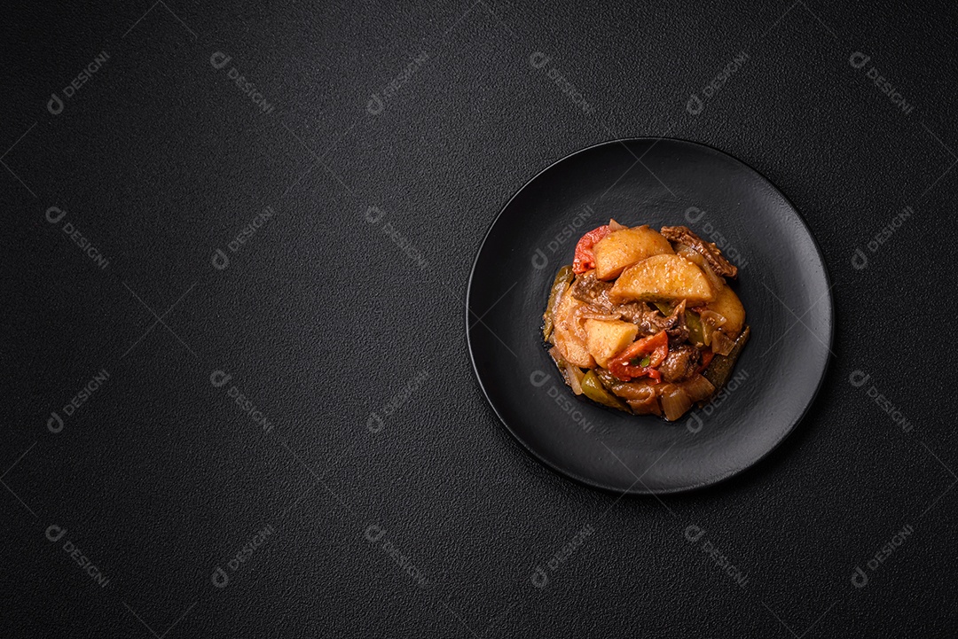 Delicioso guisado fresco de batatas, tomates, cebolas, cenouras e carne bovina com sal, especiarias e ervas sobre um fundo escuro de concreto