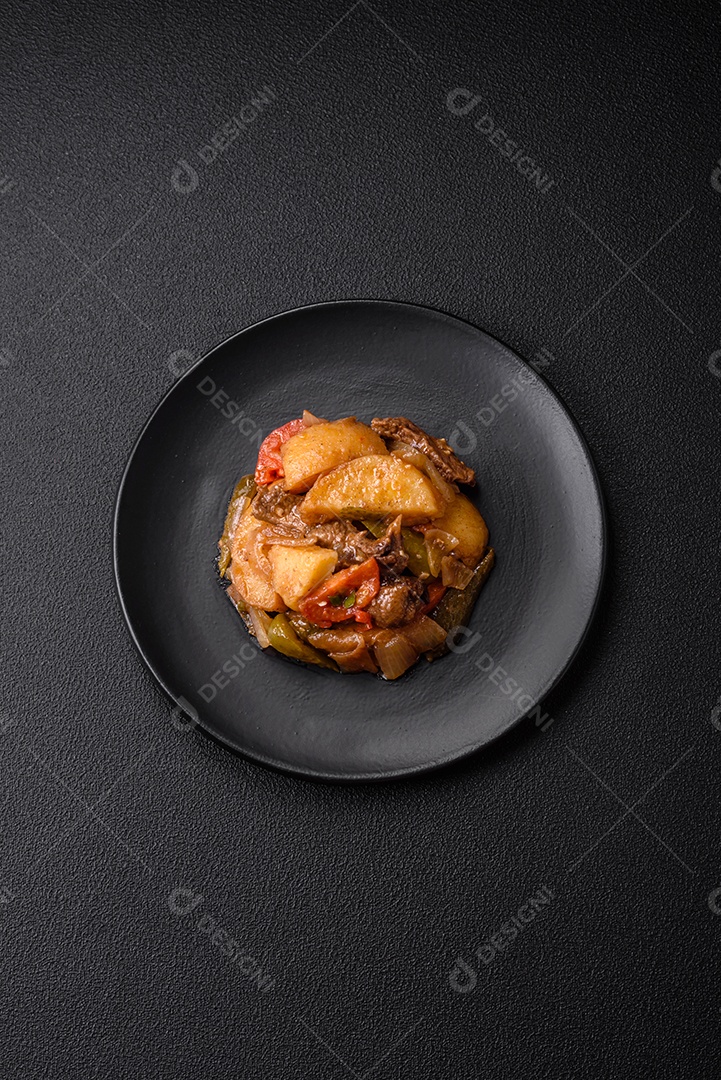 Delicioso guisado fresco de batatas, tomates, cebolas, cenouras e carne bovina com sal, especiarias e ervas sobre um fundo escuro de concreto