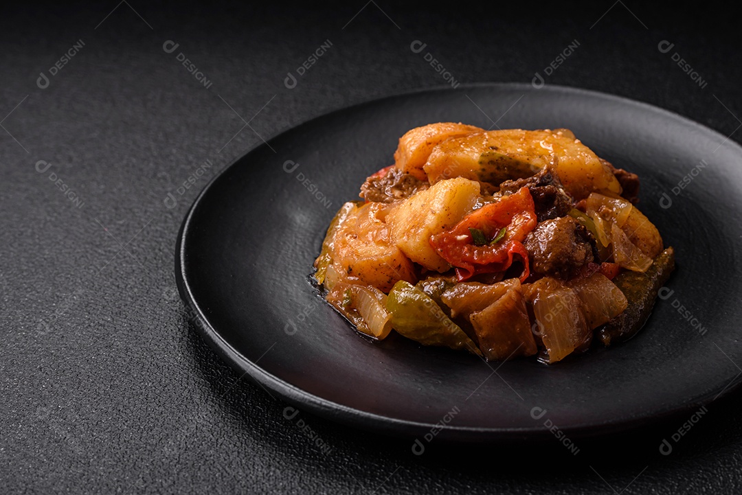 Delicioso guisado fresco de batatas, tomates, cebolas, cenouras e carne bovina com sal, especiarias e ervas sobre um fundo escuro de concreto
