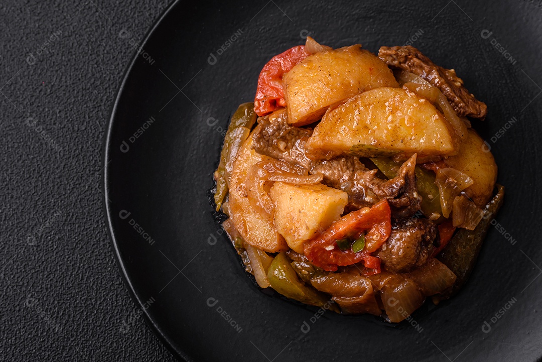 Delicioso guisado fresco de batatas, tomates, cebolas, cenouras e carne bovina com sal, especiarias e ervas sobre um fundo escuro de concreto