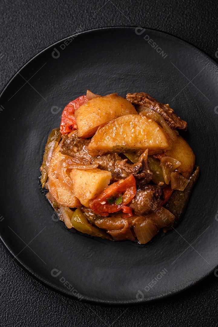 Delicioso guisado fresco de batatas, tomates, cebolas, cenouras e carne bovina com sal, especiarias e ervas sobre um fundo escuro de concreto