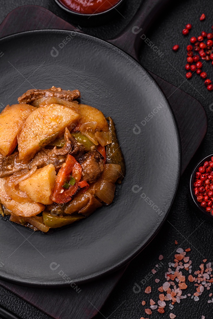 Delicioso guisado fresco de batatas, tomates, cebolas, cenouras e carne bovina com sal, especiarias e ervas sobre um fundo escuro de concreto