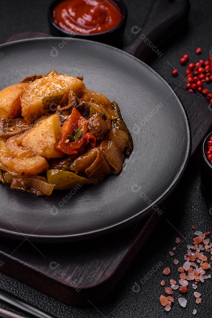 Delicioso guisado fresco de batatas, tomates, cebolas, cenouras e carne bovina com sal, especiarias e ervas sobre um fundo escuro de concreto