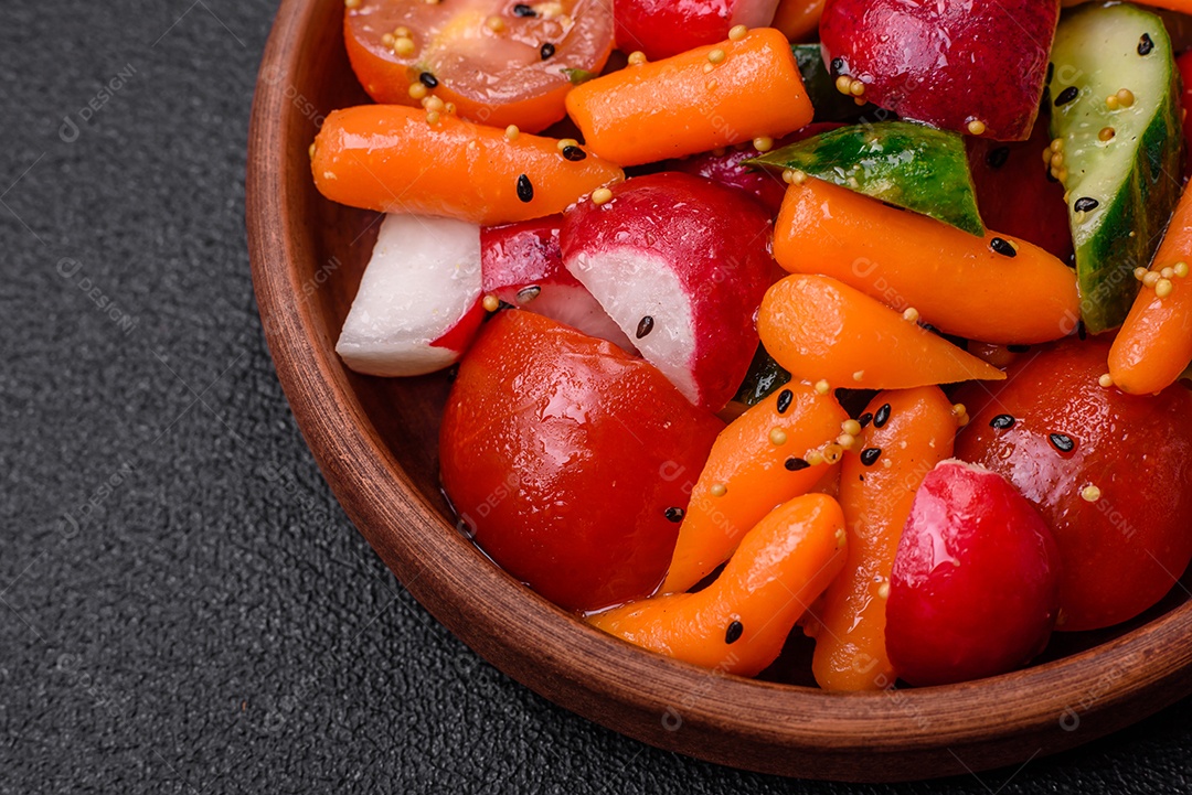 Deliciosa salada fresca e suculenta com rabanetes, tomates, cenouras, pepino, especiarias e ervas sobre um fundo escuro de concreto