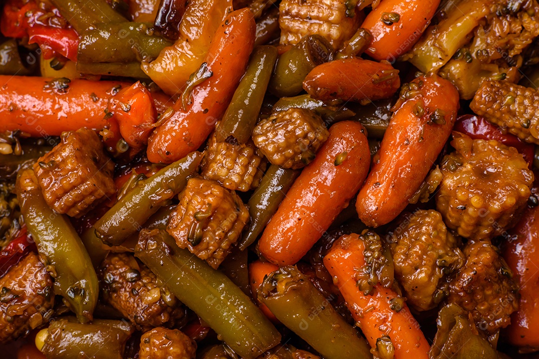 Mistura de legumes, milho, cenoura, pimentão, brócolis, cebola em molho teriyaki em uma placa de cerâmica sobre um fundo escuro de concreto