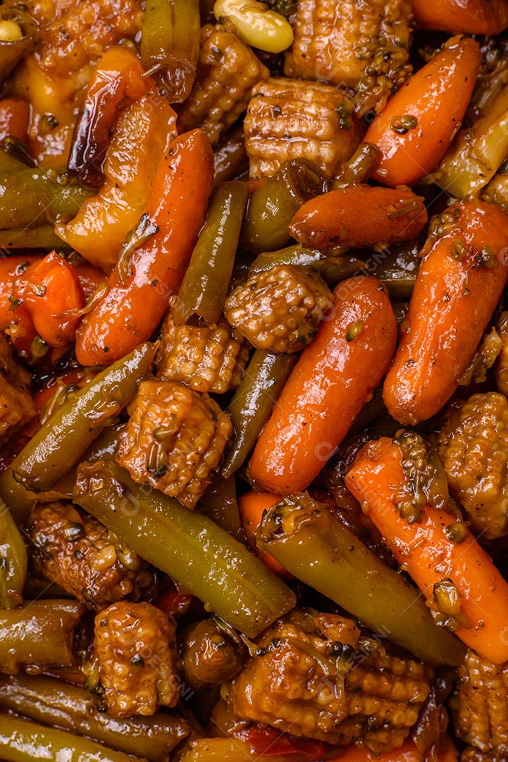 Mistura de legumes, milho, cenoura, pimentão, brócolis, cebola em molho teriyaki em uma placa de cerâmica sobre um fundo escuro de concreto