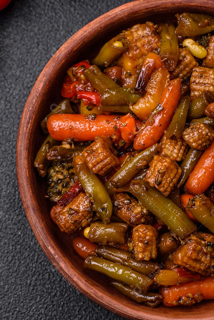 Mistura de legumes, milho, cenoura, pimentão, brócolis, cebola em molho teriyaki em uma placa de cerâmica sobre um fundo escuro de concreto