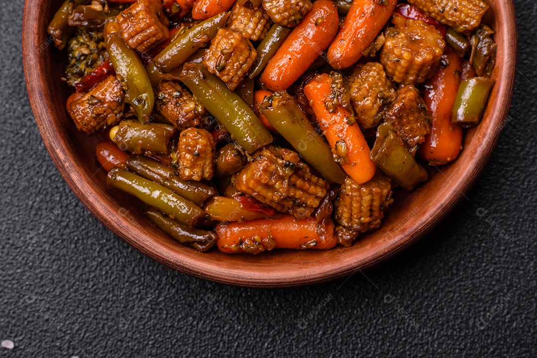 Mistura de legumes, milho, cenoura, pimentão, brócolis, cebola em molho teriyaki em uma placa de cerâmica sobre um fundo escuro de concreto