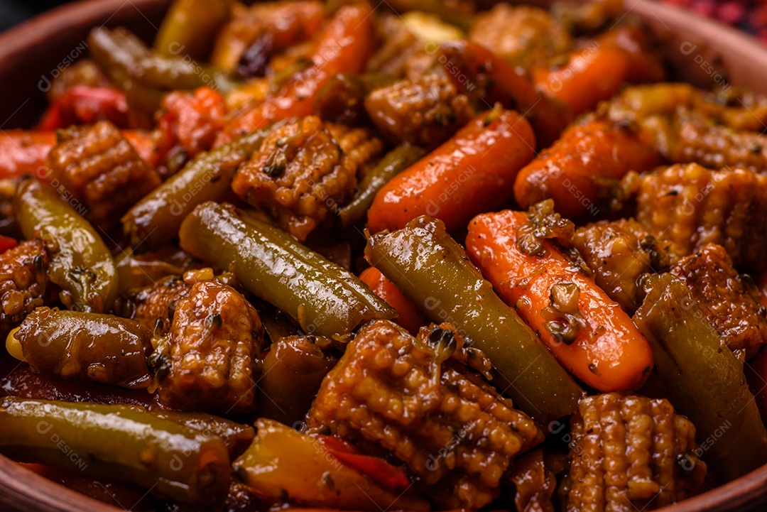 Mistura de legumes, milho, cenoura, pimentão, brócolis, cebola em molho teriyaki em uma placa de cerâmica sobre um fundo escuro de concreto