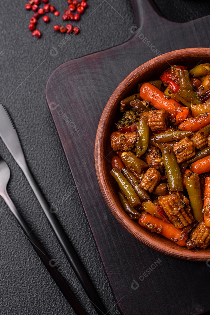 Mistura de legumes, milho, cenoura, pimentão, brócolis, cebola em molho teriyaki em uma placa de cerâmica sobre um fundo escuro de concreto