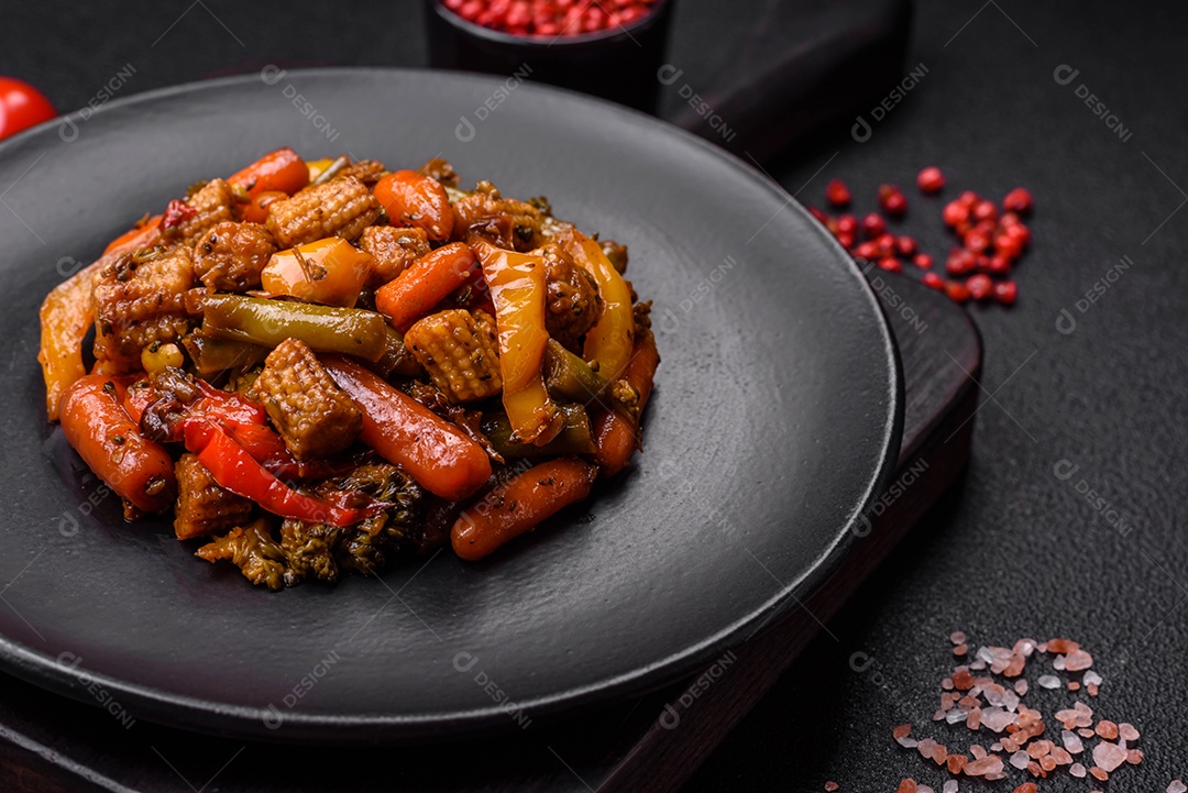 Mistura de legumes, milho, cenoura, pimentão, brócolis, cebola em molho teriyaki em uma placa de cerâmica sobre um fundo escuro de concreto