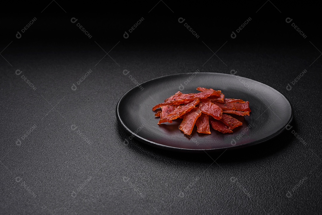 Deliciosa vitela seca ou carne seca de peru com sal, especiarias e ervas sobre um fundo escuro de concreto