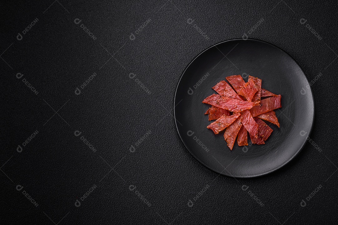 Deliciosa vitela seca ou carne seca de peru com sal, especiarias e ervas sobre um fundo escuro de concreto