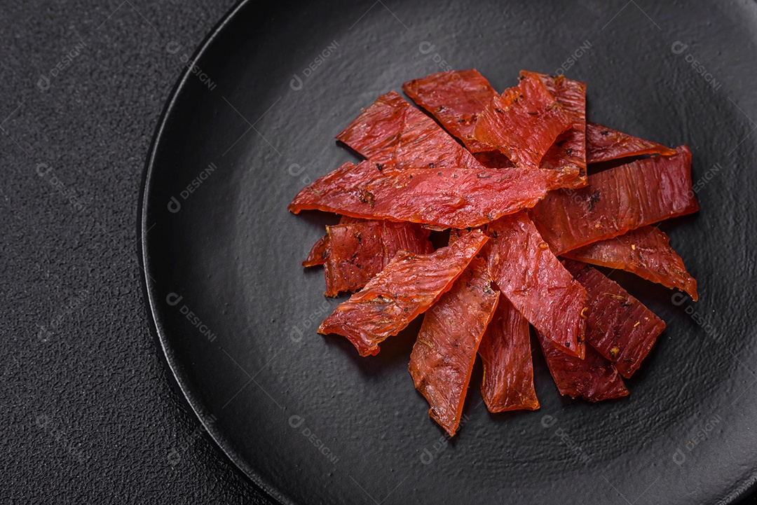 Deliciosa vitela seca ou carne seca de peru com sal, especiarias e ervas sobre um fundo escuro de concreto