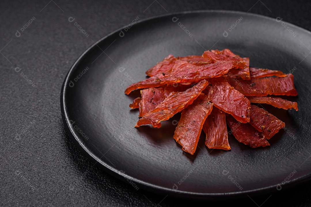 Deliciosa vitela seca ou carne seca de peru com sal, especiarias e ervas sobre um fundo escuro de concreto