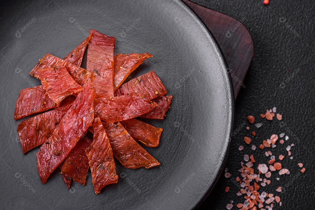 Deliciosa vitela seca ou carne seca de peru com sal, especiarias e ervas sobre um fundo escuro de concreto