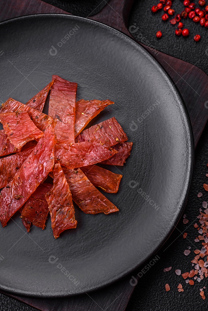 Deliciosa vitela seca ou carne seca de peru com sal, especiarias e ervas sobre um fundo escuro de concreto