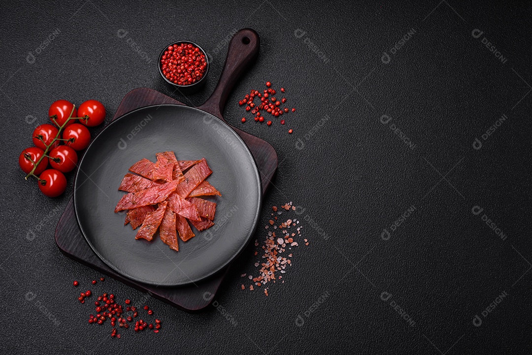 Deliciosa vitela seca ou carne seca de peru com sal, especiarias e ervas sobre um fundo escuro de concreto