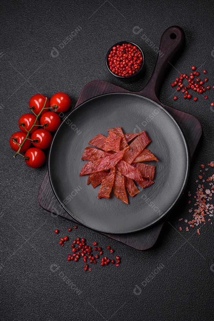 Deliciosa vitela seca ou carne seca de peru com sal, especiarias e ervas sobre um fundo escuro de concreto