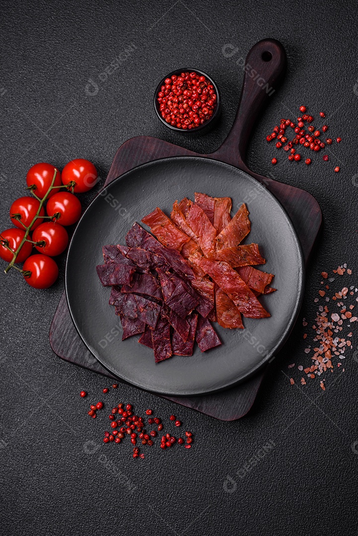 Deliciosa vitela seca ou carne seca de peru com sal, especiarias e ervas sobre um fundo escuro de concreto