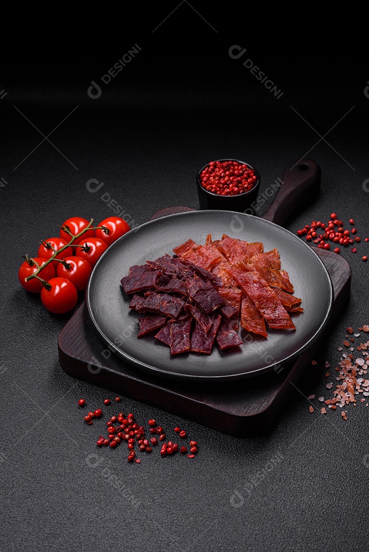 Deliciosa vitela seca ou carne seca de peru com sal, especiarias e ervas sobre um fundo escuro de concreto